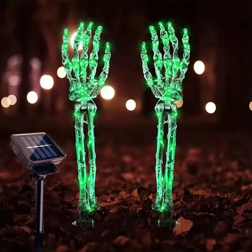 Solar Halloween skeleton hand stake light glowing green in a yard